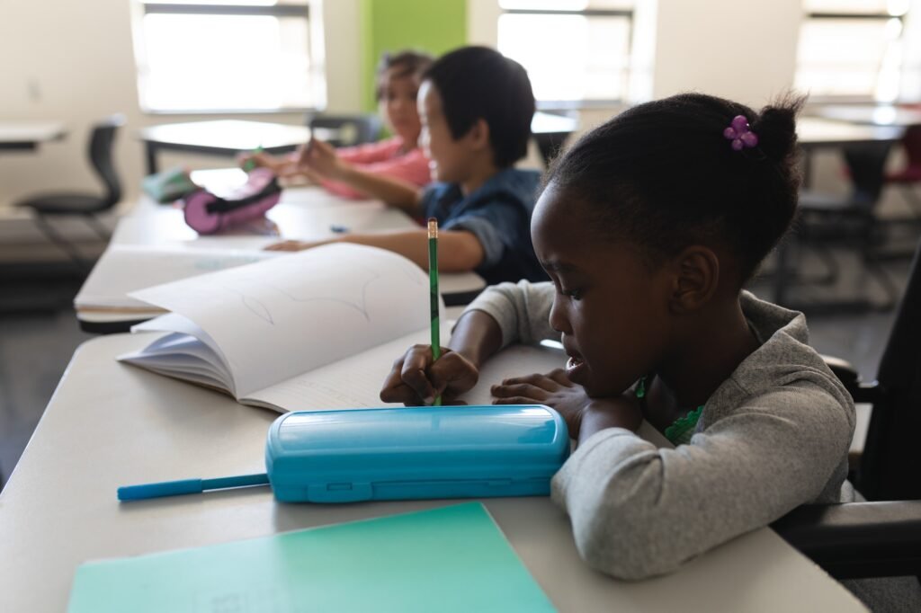 Side view of disable black schoolgirl studying and sitting at desk in classroom of elementary school